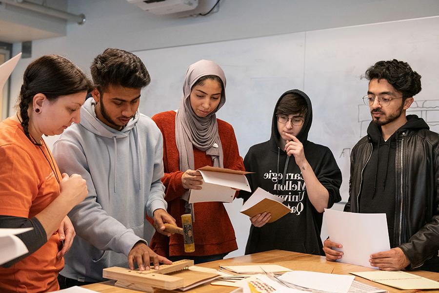 Students from Carnegie Mellon University Qatar around a table, looking at papers and a physical model.